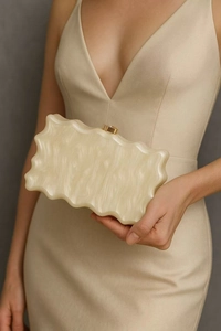 Detail of cream acrylic clutch bag with marble texture and wavy edges held by a model