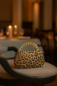 Close-up of leopard print clutch bag with bold chunky gold chain handle on a seat