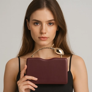 Close-up of elegant burgundy evening clutch with unique gold bird-shaped metal handle