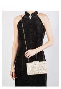 Details einer eleganten elfenbeinfarbenen Abendtasche mit Goldkette und Perlenverzierung