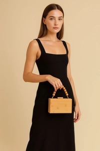 Detail of a square bamboo handbag featuring a beaded wooden handle and natural wood texture