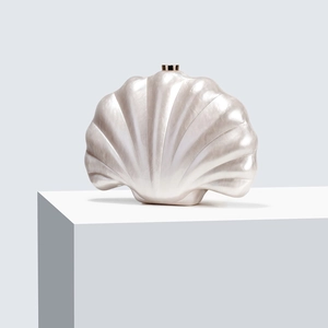 Iridescent shell-shaped acrylic evening clutch with gold metal clasp on a white pedestal