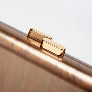 Macro detail of golden metal clasp and tortoiseshell acrylic texture on evening clutch