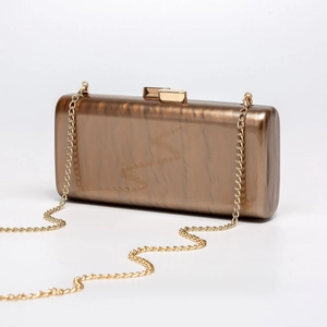 Detail of amber acrylic clutch bag with golden chain and textured shell finish