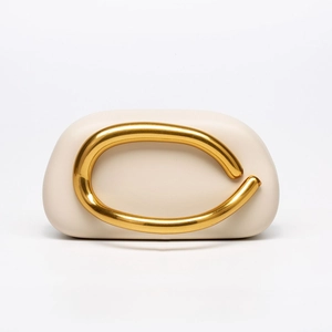 Detailed macro of minimalist off-white evening bag featuring bold gold curved metal handle