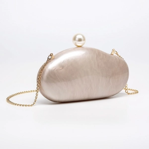 Detailed macro of champagne acrylic shell clutch bag featuring a pearl clasp and gold chain