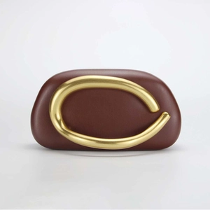 Detail of a brown leather shell clutch with large gold C-shaped metal handle and smooth finish