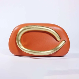Detail of orange shell-shaped acrylic clutch with u-shaped gold metal handle for wedding