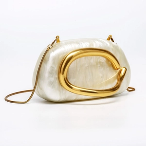 Detailed view of white pearlescent acrylic shell bag with gold organic shaped metal handle