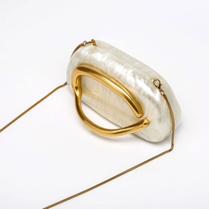 Close-up of pearl white acrylic clutch with artistic gold handle and snake chain