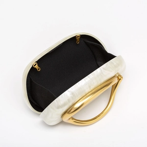 Detail of acrylic shell clutch bag featuring marbled texture and golden metal handle