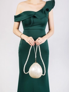 Detail of egg-shaped acrylic shell clutch with pearl handle worn by model in green dress