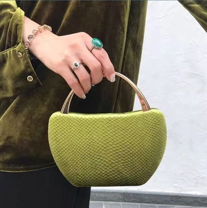 Detail of green snake pattern evening bag with curved gold handle held by model