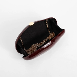 Detailed interior of glossy burgundy patent leather clutch with a fine gold chain strap