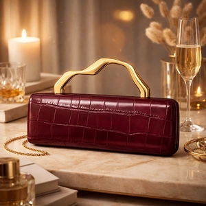 Detail of burgundy crocodile-embossed clutch with wavy gold handle on marble
