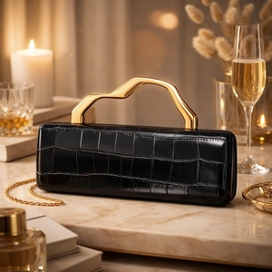 Detail of black crocodile texture bag with sculpted gold handle on marble surface