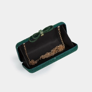 Detailed view of emerald rhinestone evening clutch with bow clasp and golden chain strap