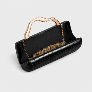 Close-up of black crocodile pattern clutch bag with wavy gold metal handle and chain