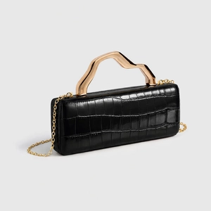Macro shot of black crocodile embossed clutch with artistic golden wavy metal handle