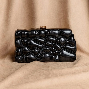 Schwarze Acryl-Abendtasche in Muschelform mit Goldverschluss auf beigem Samthintergrund