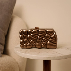 Detail der kreativen bronzefarbenen Acryl-Clutch mit Faltenstruktur auf weißem Marmor