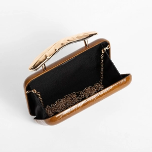 Detail view of glossy brown PU evening clutch with unique wavy gold metal handle and chain