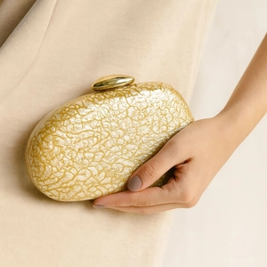 Detail of gold marble acrylic evening bag with metallic oval clasp and hand-held texture