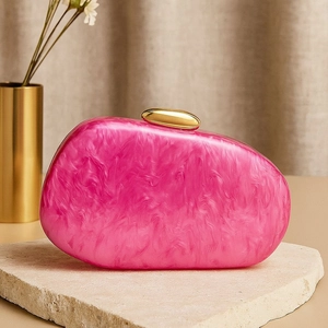 Detail of pink marble acrylic shell clutch with gold metal clasp on stone background