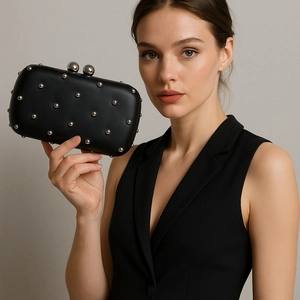 Pochette noire pour femme avec clous argentés et fermoir sphérique tenue par un mannequin