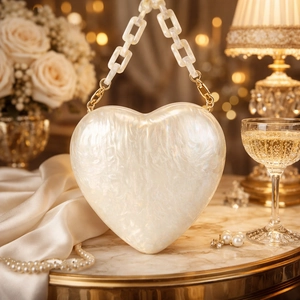 Heart-shaped pearl white acrylic evening clutch with thick chain on marble background