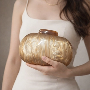 Detail of marble pattern acrylic clutch bag with amber clasp held by model in white dress