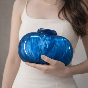Close-up of blue marble acrylic oval clutch bag held by model wearing a white dress
