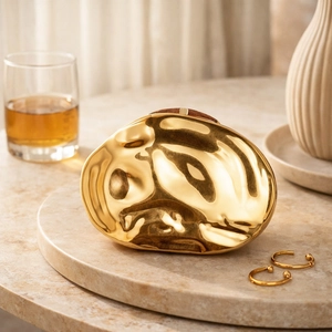 Luxury gold shell evening bag with fluid metal texture on a minimalist stone tray