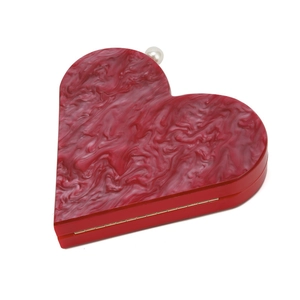 Detail of red heart-shaped acrylic clutch with pearl clasp and gold metal hinges