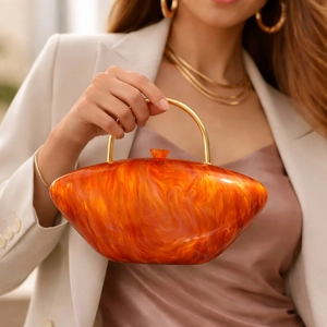 Detail of orange acrylic clutch with marble pattern and golden round metal handle