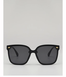 Detailed close-up of the golden metal logo on these black square oversized sunglasses