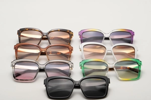 Flat lay of oversized square sunglasses in seven assorted gradient colors and frame styles