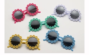 Flat lay of colorful daisy-shaped kids sunglasses in pink, purple, yellow, and blue