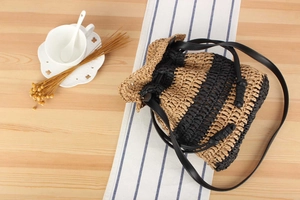 Detail of woven straw bucket bag with black stripes and leather strap on a table