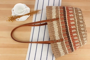 Vue de dessus d'un sac cabas en paille rayé avec anses en cuir sur une table en bois