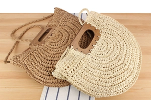 Detail view of semi-circular straw bag with rectangle wood handle and detachable strap