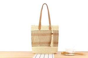 Détail de la texture tressée et de la poignée en cuir marron avec franges sur un sac en paille