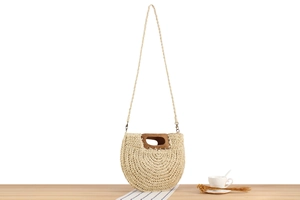 Detail of semi-circular straw bag featuring a dark wooden handle and woven shoulder strap