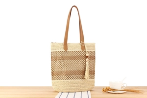 Gros plan du sac cabas en paille tissée avec pompon brun et anses en cuir synthétique