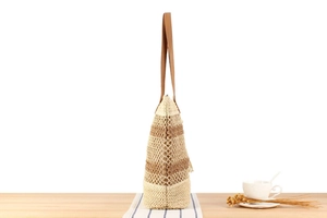 Détail d'un sac cabas en paille tressée avec anses en cuir marron sur nappe rayée bleue