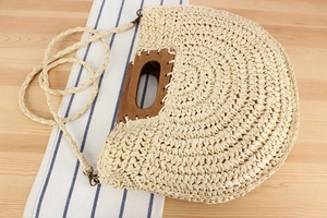 Detail of beige straw handbag with semi-circular wooden handles and detachable strap