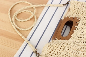Detail of cream handmade crochet straw bag featuring square wooden handles and metal hooks