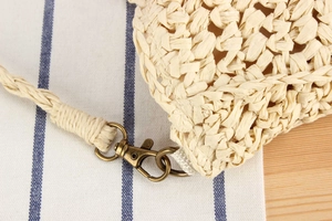 Detailed close-up of straw bag lobster clasp and zipper on rustic wood background