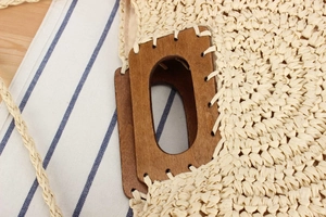 Detail of hand-woven straw tote with red-brown rectangular wooden handle and slim strap