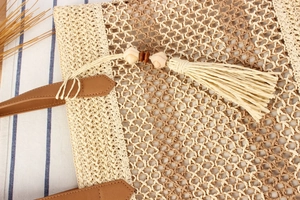 Détail d'un sac cabas en paille tressée avec pompons beiges, perles en bois et anses en cuir